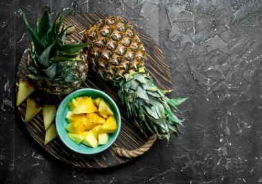 Dilim ananas bir kase ve bir tepsi üzerinde bütün taze ananas. Rustik siyah arka plan üzerine