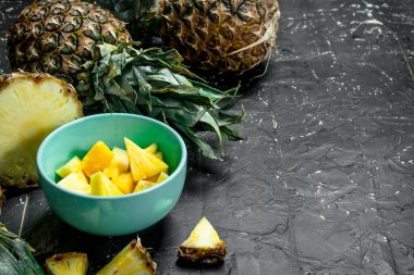 Bir kase içinde olgunlaşmış taze ananas parçaları. Rustik siyah arka plan üzerine