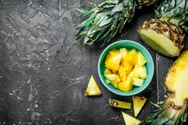 Bir kase içinde olgunlaşmış taze ananas parçaları. Rustik siyah arka plan üzerine
