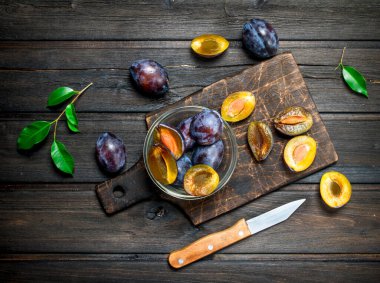 Bir bıçak ile kesme tahtası üzerinde bir kapta taze Erik parçalarını. Ahşap arka plan üzerinde