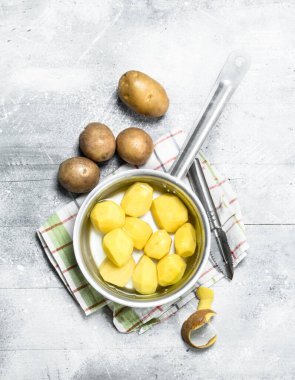 Soyulmuş patates peçete üzerinde bir tencerede. Beyaz rustik arka plan üzerinde