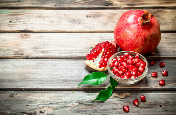 Семена граната в миске и сочный гранат с листьями. На деревянном фоне
