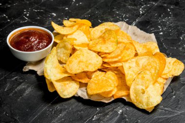 Eski kağıt domates soslu patates cipsi. Rustik siyah arka plan üzerine.