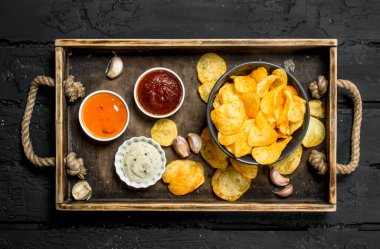 Soslar ahşap tepsi içinde patates cipsi. Rustik siyah arka plan üzerine.