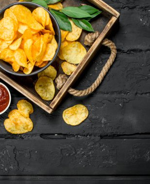 Soslar ahşap tepsi içinde patates cipsi. Rustik siyah arka plan üzerine.