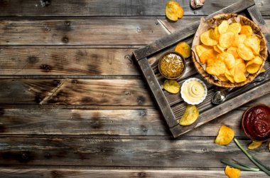 Bir sepet farklı sos ve patates cipsi. Ahşap bir arka plan üzerinde.