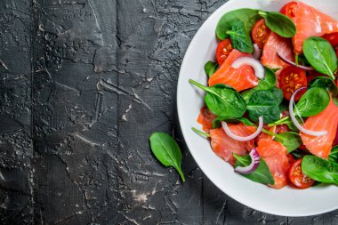 Balık salatası. Dilim somon, domates ve limon suyu ile ıspanak salatası. Rustik siyah arka plan üzerine.