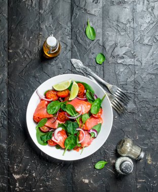 Balık salatası. Dilim somon, domates ve limon suyu ile ıspanak salatası. Rustik siyah arka plan üzerine.