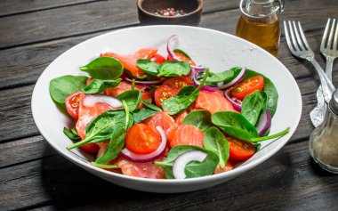 Balık salatası. Dilim somon, domates ve limon suyu ile ıspanak salatası. Ahşap bir arka plan üzerinde.