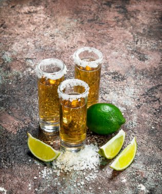 Tekila shot bardak tuz ve limon dilimleri içinde. Rustik arka plan üzerinde