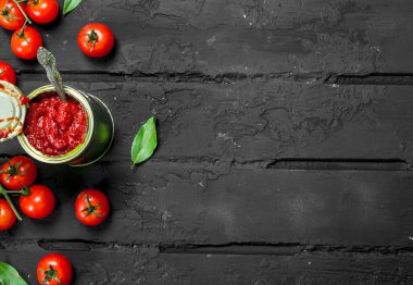 Bir kaşık, yaprak ve domates ile bir teneke teneke domates sosu. Siyah rustik arka plan üzerinde