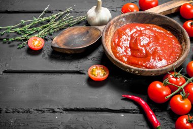 Domates sosu kaşık, otlar ve biber kase. Rustik siyah arka plan üzerine