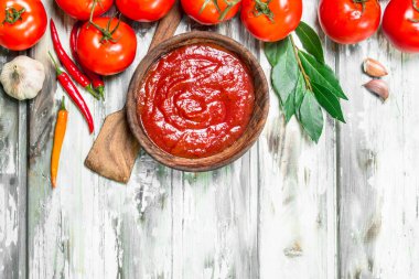 Kepçe, defne yaprağı ve acı biber kase domates sosu. Ahşap arka plan üzerinde