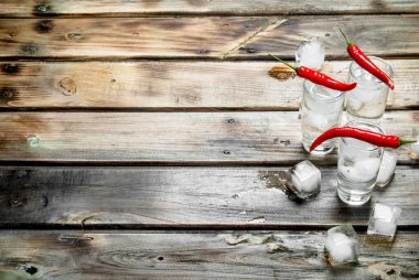 Bir içki kadehi ve kırmızı acı biber buzlu votka. Ahşap arka plan üzerinde