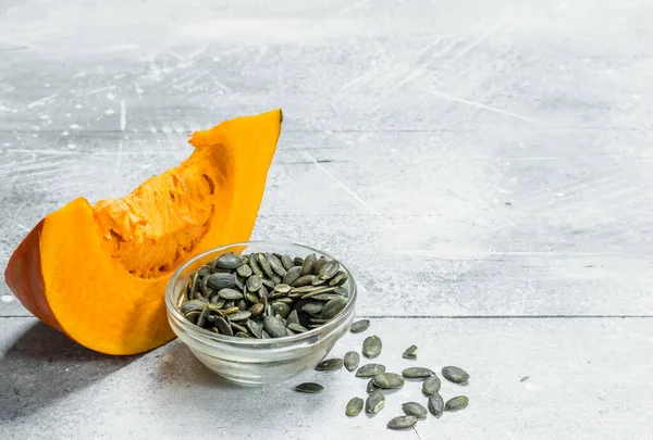 Stock image Pumpkin seeds in a bowl and a piece of ripe pumpkin. On rustic background