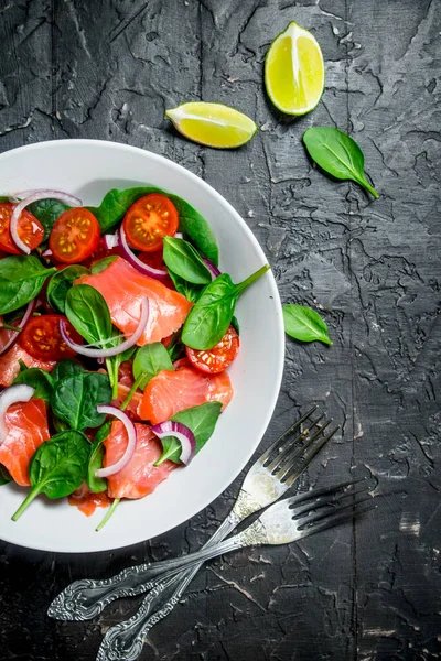 Balık salatası. Dilim somon, domates ve limon suyu ile ıspanak salatası. Rustik siyah arka plan üzerine.