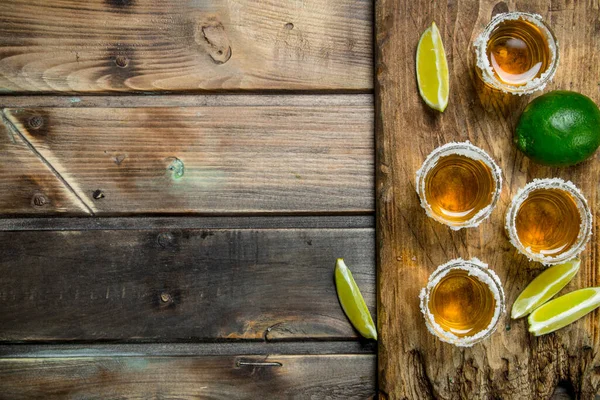 stock image Tequila in a shot glass on a cutting Board with slices of lime. On wooden background