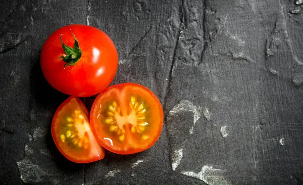 stock image Pieces and a whole tomato. On black rustic background