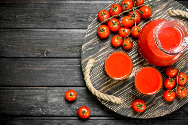 stock image Tomato juice in a jug and glasses on tray. On black wooden background