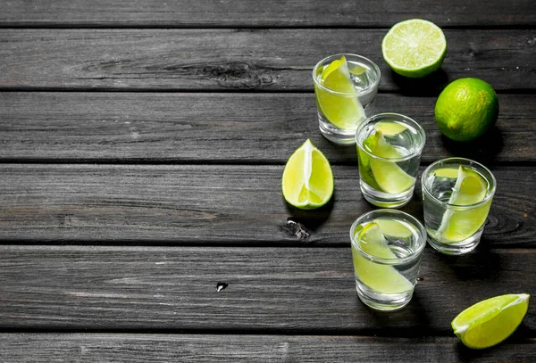 stock image Vodka in a shot glass and lime slices. On wooden background