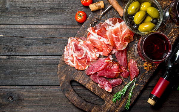 Antipasto background. Different meat snacks with red wine. On a wooden background.