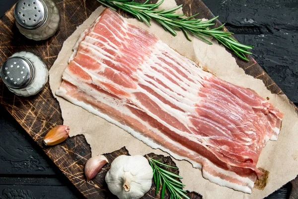 stock image Raw bacon with rosemary and spices. On black rustic background.