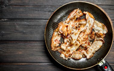 Bir tavada kızarmış domuz pastırması. Ahşap bir arka plan üzerinde.