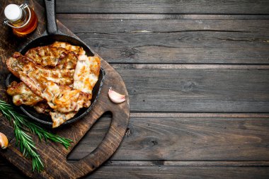 Baharat ve biberiye ile bir tavada kızarmış domuz pastırması. Ahşap bir arka plan üzerinde.