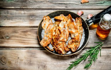 Zeytin yağı ve biberiye ile kızarmış domuz pastırması. Ahşap bir arka plan üzerinde.