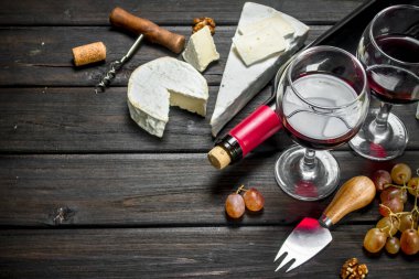 Brie peyniri ile kırmızı şarap, fındık ve üzüm. Ahşap bir arka plan üzerinde.