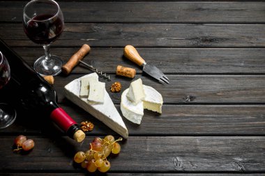 Brie peyniri ile kırmızı şarap, fındık ve üzüm. Ahşap bir arka plan üzerinde.