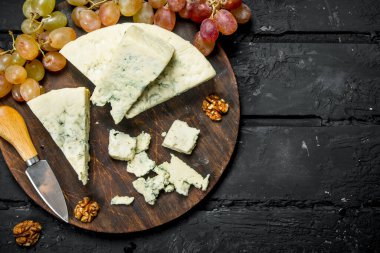 Mavi peynir üzüm ile ahşap bir gemide. Siyah bir rustik arka planda.