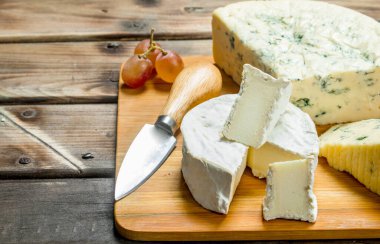 Mavi ve brie peyniri bir bıçak ile kesme tahtası üzerinde. Ahşap bir arka plan üzerinde.