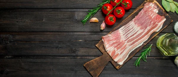 stock image Raw bacon with tomatoes and herbs. On a wooden background.