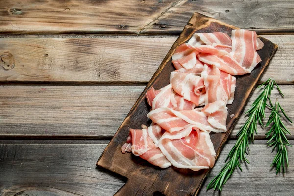 stock image Raw bacon with fragrant rosemary. On a wooden background.