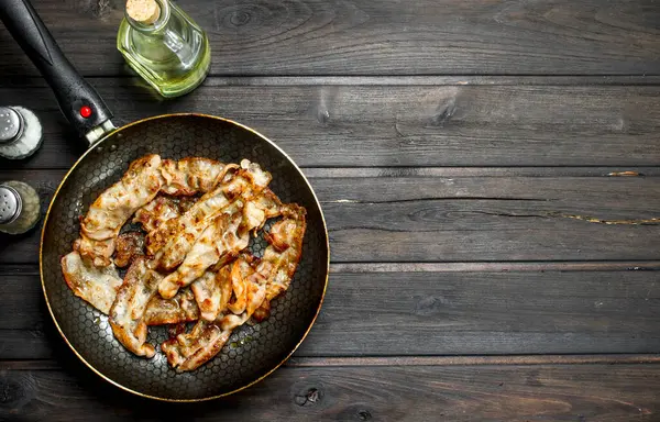 stock image Fried bacon in a pan with spices. On a wooden background.