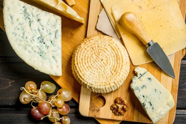 stock image Assortment of different cheeses with grapes and walnuts. On a wooden background.