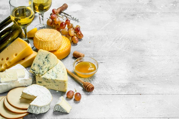 stock image Assortment of types of cheese with white wine and honey. On a rustic background.