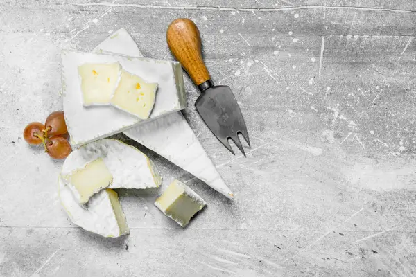 stock image Brie cheese with grapes and knife. On a rustic background.