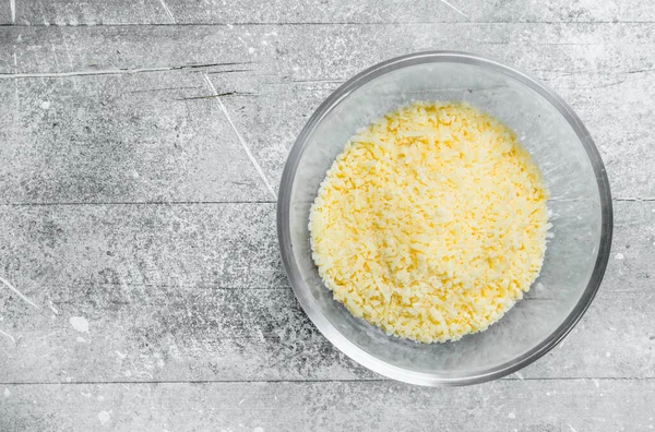 stock image Grated cheese in a glass bowl. On a rustic background.