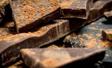 Çikolata dilimleri kakao tozu serpilir. Siyah rustik arka plan üzerinde.