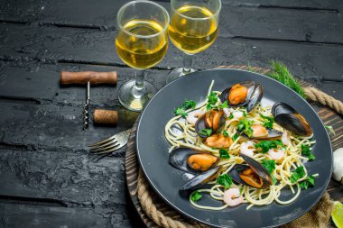 Akdeniz yemekleri. Deniz mahsulleri spagetti istiridye ve beyaz şarap. Siyah bir rustik arka planda.