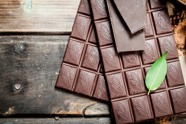 stock image Chocolate bars with green leaf. On a wooden background.