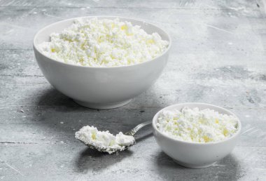 Bir kaşık ile bir kase süzme peynir. Rustik bir arka plan üzerinde.