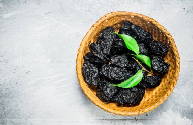 Yeşil yaprakları ile bir kase kuru erik. Rustik bir arka plan üzerinde.