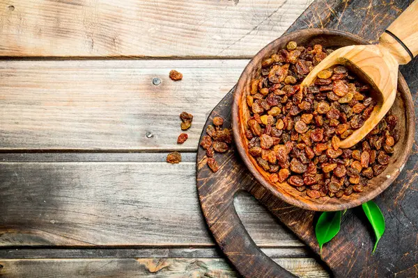 stock image Raisins in a bowl with a wooden scoop. On a Wooden background.