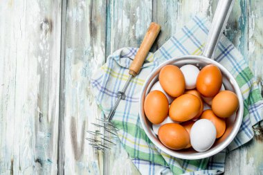 Peçete üzerinde bir çırpma teli ile bir tencerede yumurta. Rustik bir arka plan üzerinde.