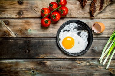 Ekmek, domates ve yeşil soğan ile bir tavada kızarmış yumurta. Ahşap bir arka plan üzerinde.