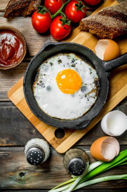 Ekmek, domates ve yeşil soğan ile bir tavada kızarmış yumurta. Ahşap bir arka plan üzerinde.