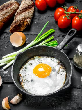Sahanda yumurta ekmek ve domates ile bir tavada. Rustik siyah arka plan üzerine.